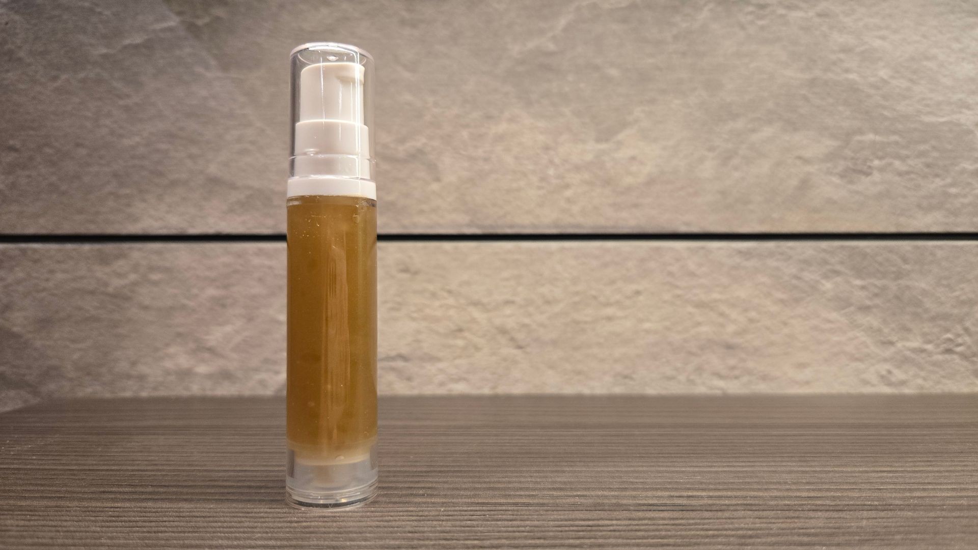 Clear pump bottle with brown liquid on a wooden surface, set against a textured stone background.