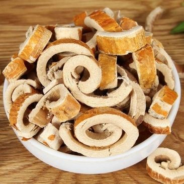 Bowl filled with dried, spiral-cut slices of a brown root on a wooden surface.