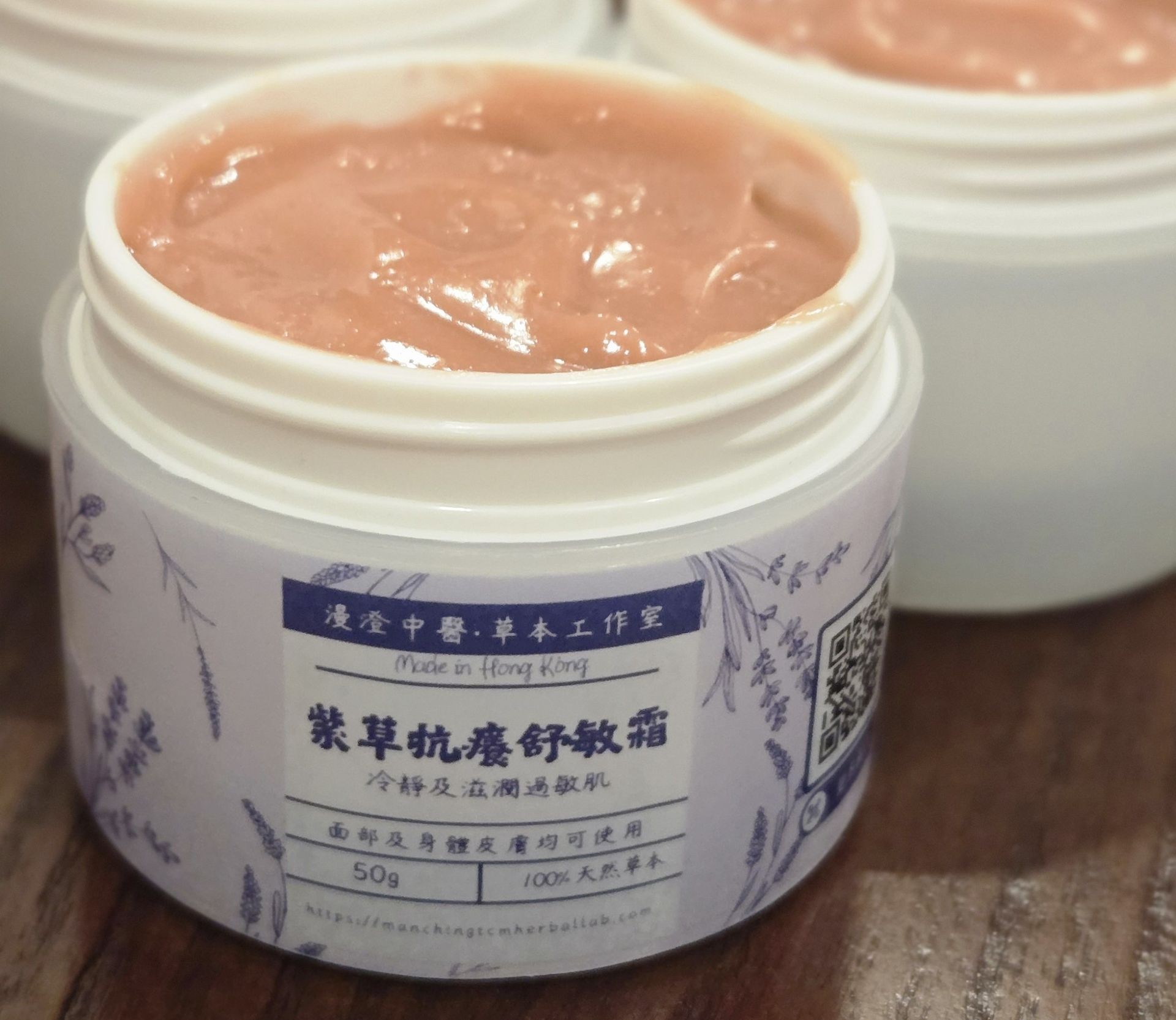 Open jar of pink herbal cream with Chinese text and lavender illustrations on the label.
